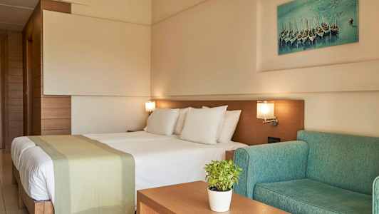 Et hotellrom med en dobbeltseng, grønn sofa og veggkunst. (AI-generert tekst)