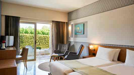 Hotellrom med to senger, sittegruppe, vindu mot grønne omgivelser. (AI-generert tekst)