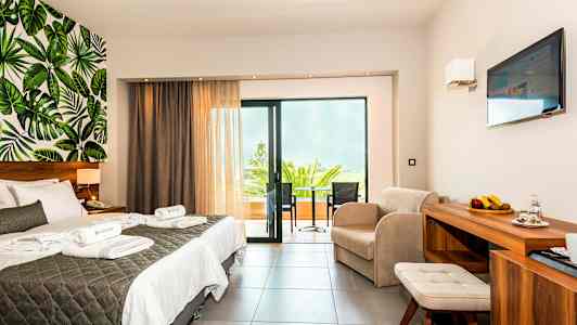 Et hotellrom med dobbeltseng, sittegruppe, balkong og veggdekor med bladmotiv. (AI-generert tekst)