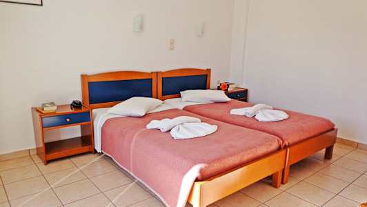 To enkeltsenger med brettede håndklær og rosa sengeteppe, to nattbord og flisgulv i et hotellrom. (AI-generert tekst)