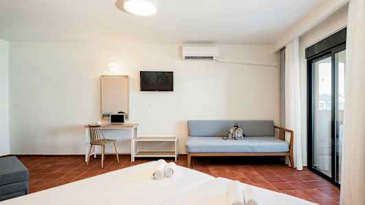 Et hotellrom med en seng, sofa, skrivebord og en balkong med glassdører. (AI-generert tekst)