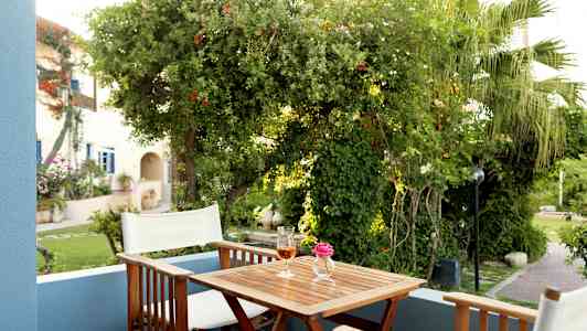 En terrasse med to stoler, et bord med en rosa blomst i en vase og et glass drikke, omgitt av frodig vegetasjon. (AI-generert tekst)