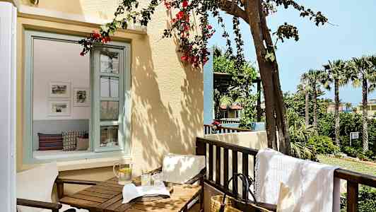 En balkong med hageutsikt, bord og stoler samt en vannkaraff med glass. (AI-generert tekst)