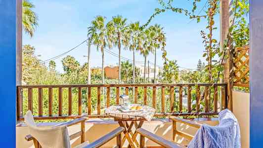 Balkong med to stoler, et bord og utsikt over palmer. (AI-generert tekst)