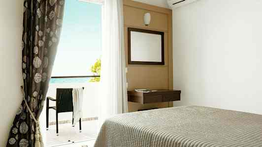 Hotellrom med seng, speil, gardiner og balkong med utsikt mot havet. (AI-generert tekst)