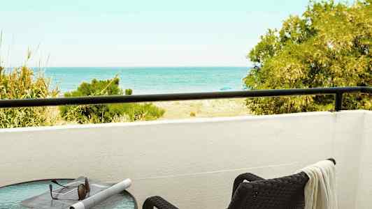 En balkong med utsikt mot havet, et bord med solbriller og en avis samt en stol med et håndkle. (AI-generert tekst)