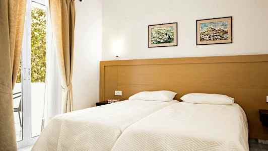 Et soverom med to enkeltsenger, en treramme, lyse sengetøy og to bilder over sengene. (AI-generert tekst)