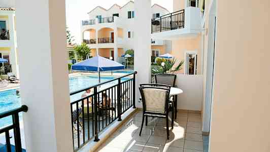 En balkong med møbler, utsikt mot et basseng og oransje bygninger. (AI-generert tekst)