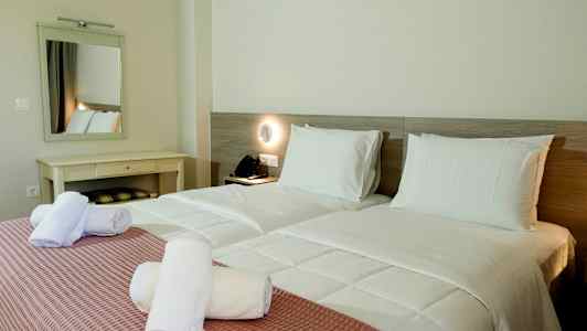 To enkeltsenger med hvitt sengetøy og rosa sengeteppe, samt hvite håndklær rullet sammen oppå. (AI-generert tekst)