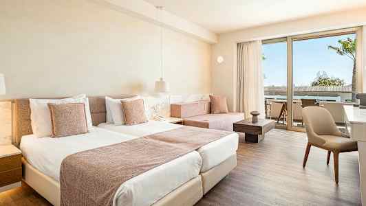 Rom med lys innredning, to senger og en sittegruppe ved en terrasse. (AI-generert tekst)