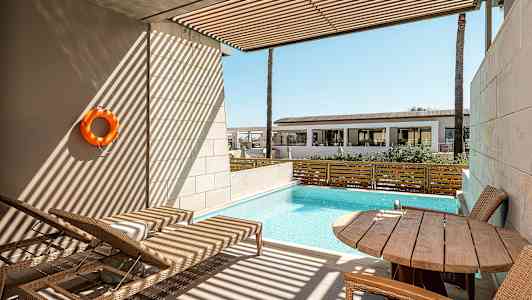 En privat terrasse med utsikt over et lite basseng, solsenger og et bord med stoler. (AI-generert tekst)