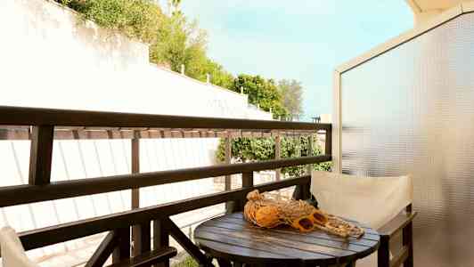En balkong med et bord, stoler og utsikt over grøntområder. (AI-generert tekst)