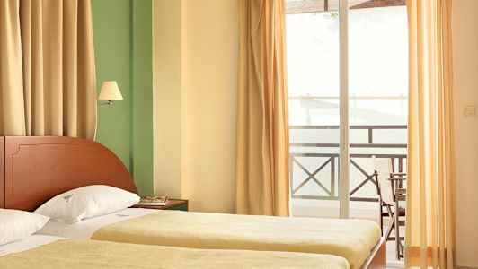 Et hotellrom med to enkeltsenger, gardiner og en balkong. (AI-generert tekst)