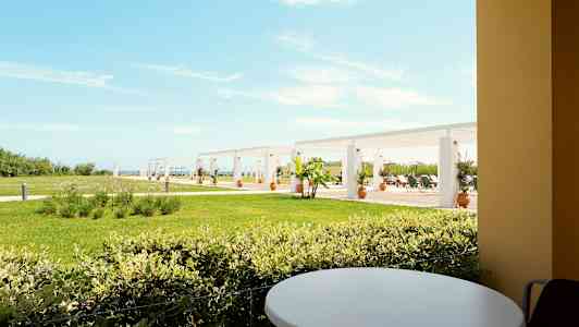 Utsikt fra en terrasse med et rundt bord mot en plen og pergola i bakgrunnen. (AI-generert tekst)