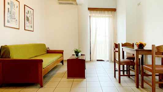 En stue med sofa, sofabord og spisebord med stoler. Lyse vegger og gardiner. (AI-generert tekst)