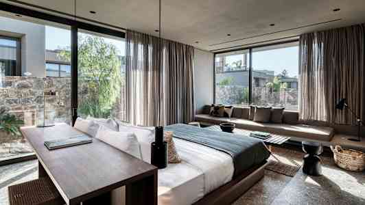 Bilde av et moderne hotellrom med stor seng, skrivebord og sofa, samt vinduer med utsikt mot en frodig gårdsplass. (AI-generert tekst)