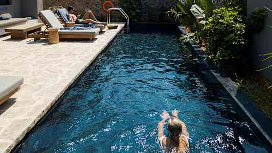 Person svømmer i et basseng med solsenger ved siden av. (AI-generert tekst)