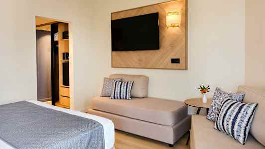 Et hotellrom med sofa, seng og TV på veggen. (AI-generert tekst)