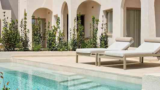 Bilde av to solsenger ved et basseng, med hvite bygninger og grønne planter i bakgrunnen. (AI-generert tekst)