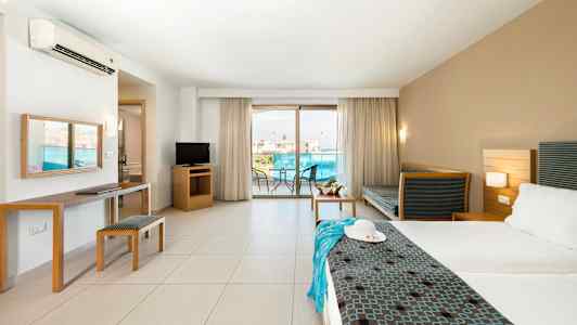 Et hotellrom med en dobbeltseng, sittemøbler, TV og en balkong med utsikt. (AI-generert tekst)