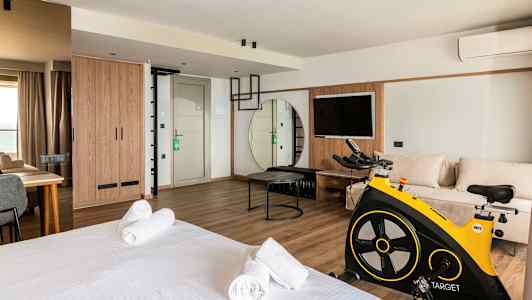 Et moderne hotellrom med seng, sittegruppe, trimsykkel og TV. (AI-generert tekst)