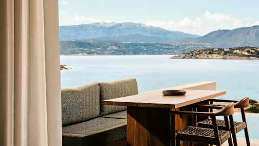 Utsikt over et trebord og stoler med havet og fjell i bakgrunnen. (AI-generert tekst)