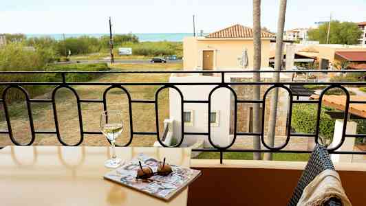 Balkong med bord, vinglass og blad, utsikt over plen og hav. (AI-generert tekst)