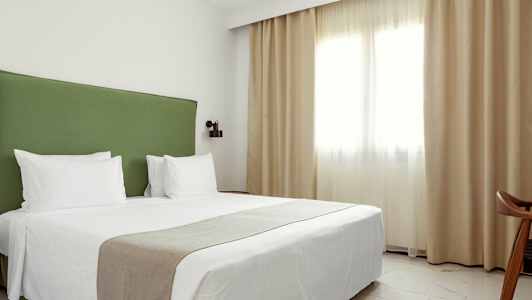 Et hotellrom med dobbeltseng, grønn sengegavl og hvitt sengetøy. (AI-generert tekst)