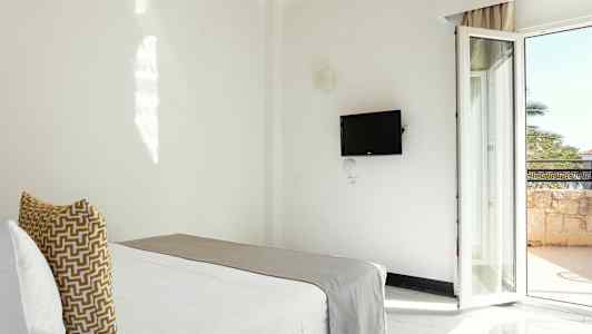 Et hotellrom med en seng, en vegghengt TV og en balkongdør. (AI-generert tekst)