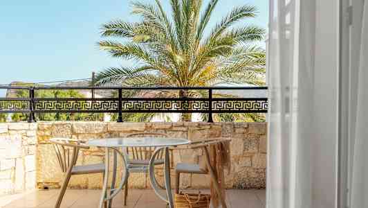 Utsikt over en solrik terrasse med bord og stoler, mot en palme og blå himmel. (AI-generert tekst)