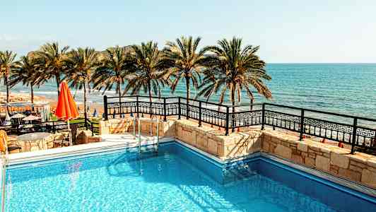 Bilde av et basseng med havet og palmer i bakgrunnen. (AI-generert tekst)