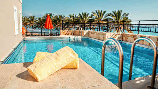 Et svømmebasseng omgitt av palmetrær med et gult håndkle i forgrunnen. (AI-generert tekst)