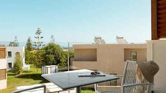 En balkong med utemøbler og utsikt over en grønn hage omgitt av bygninger. (AI-generert tekst)