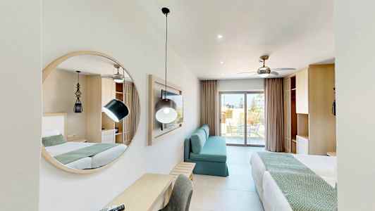 Et moderne hotellrom med to senger, et speil, en sofa og et skrivebord. En balkong er synlig i bakgrunnen. (AI-generert tekst)