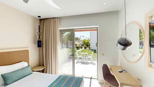 Soverom med seng, skrivebord og glassdør til terrasse med utemøbler. (AI-generert tekst)