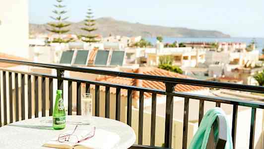 Bord med bok, briller og drikke på balkong med utsikt over hus og hav. (AI-generert tekst)