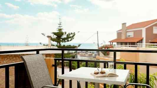 En balkong med et bord, en stol og utsikt mot havet. (AI-generert tekst)