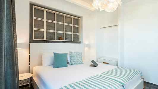 Et lyst og moderne hotellrom med en dobbeltseng, sengelamper, hvite vegger og dekorative detaljer. (AI-generert tekst)