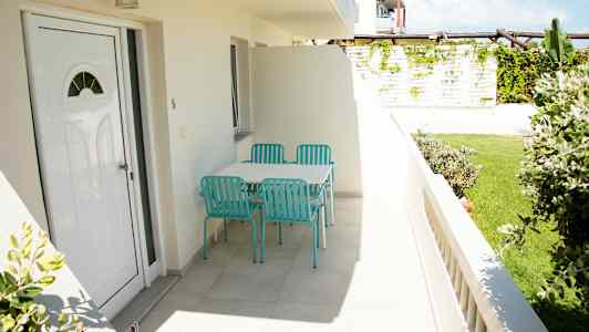 Bilde av en terrasse med et bord og fire turkise stoler, omgitt av grøntområder. (AI-generert tekst)