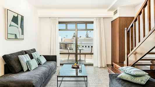 En stue med en sofa, et bord og en trapp, samt en balkong med utsikt. (AI-generert tekst)