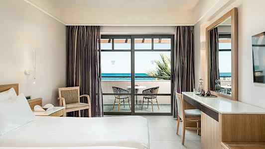 Hotellrom med seng, skrivebord og balkong med havutsikt. (AI-generert tekst)