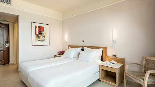 Et hotellrom med en dobbeltseng, nattbord og stol. (AI-generert tekst)