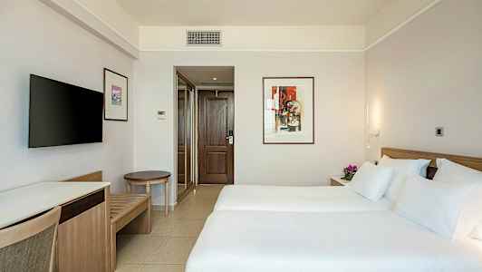 Hotellrom med to enkeltsenger, dekorativt kunstverk på veggen og TV. (AI-generert tekst)