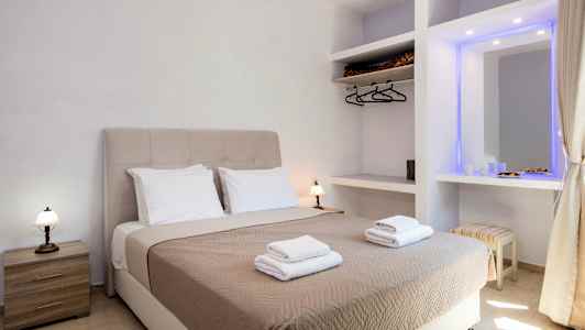 Et hotellrom med en dobbeltseng utstyrt med beige sengeteppe og to sett med håndklær, samt sidebord og garderobe. (AI-generert tekst)