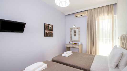 Bilde av et rom med to enkeltsenger, sengetøy og puter, en veggmontert TV, et speil med belysning over et skrivebord og et vindu med lyse gardiner. (AI-generert tekst)