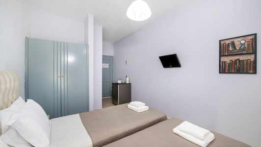 Hotellrom med to enkeltsenger, et garderobeskap, et lite kjøleskap og en veggmontert TV. (AI-generert tekst)