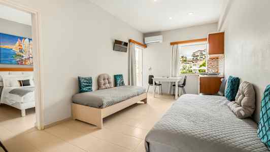 Et hotellrom med to enkeltsenger, et bord og stoler, samt utsikt gjennom vinduet. (AI-generert tekst)