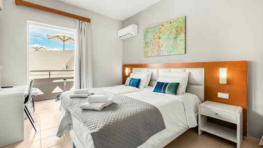 Bilde av et hotellrom med to senger, en balkong med parasoller og et maleri på veggen. (AI-generert tekst)