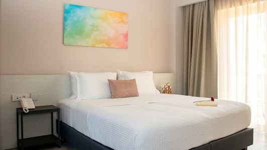 Et soverom med en dobbeltseng, hvitt sengetøy og et fargerikt maleri på veggen. (AI-generert tekst)