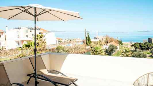 Solstoler og parasoll på en terrasse med utsikt over havet og omkringliggende bygninger. (AI-generert tekst)